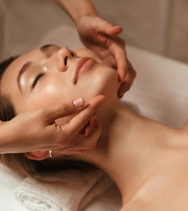Hands applying cream or mask to face during facial treatment.